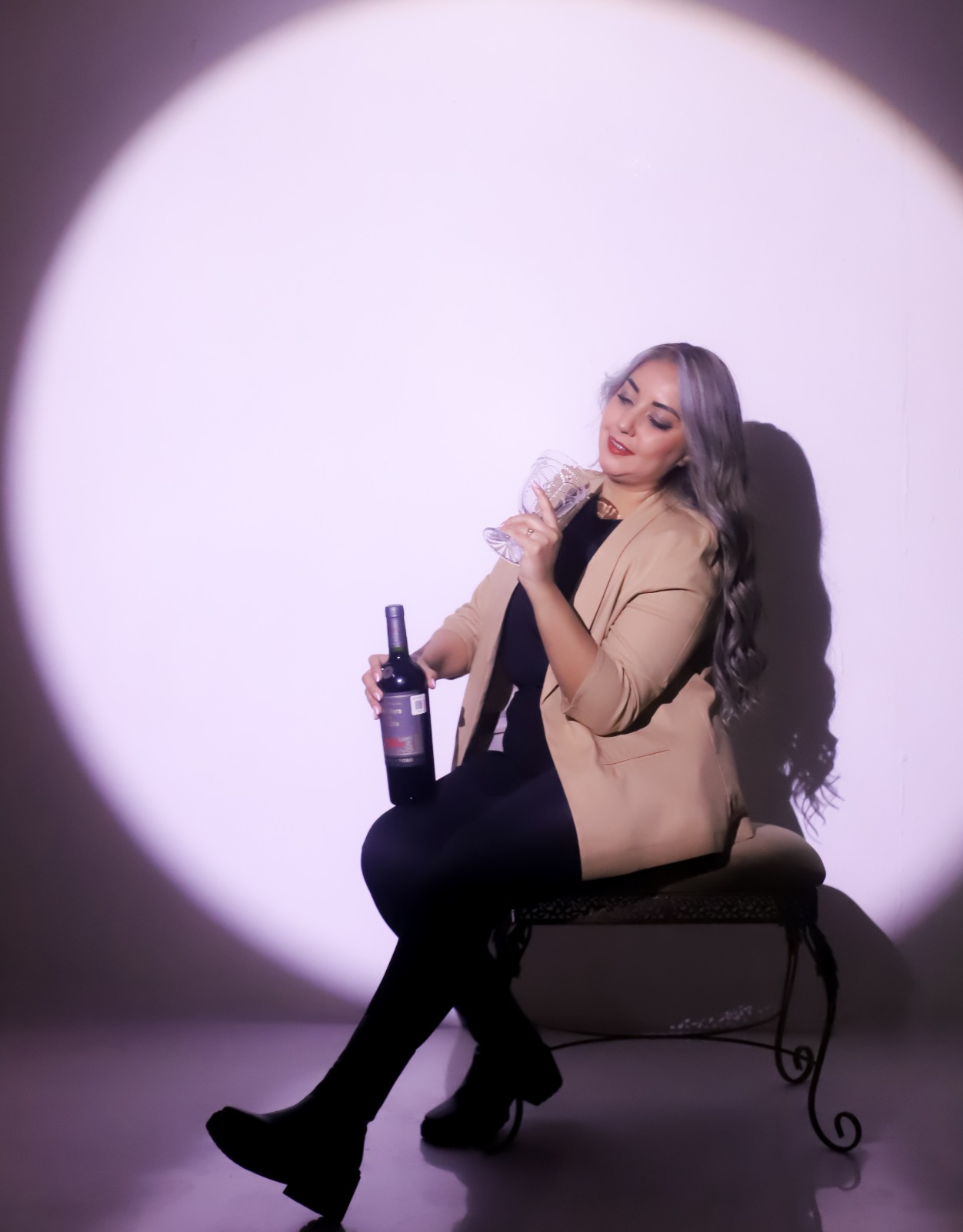 Retrato de estudio con foco de luz y una mujer con blazer sosteniendo una copa.
