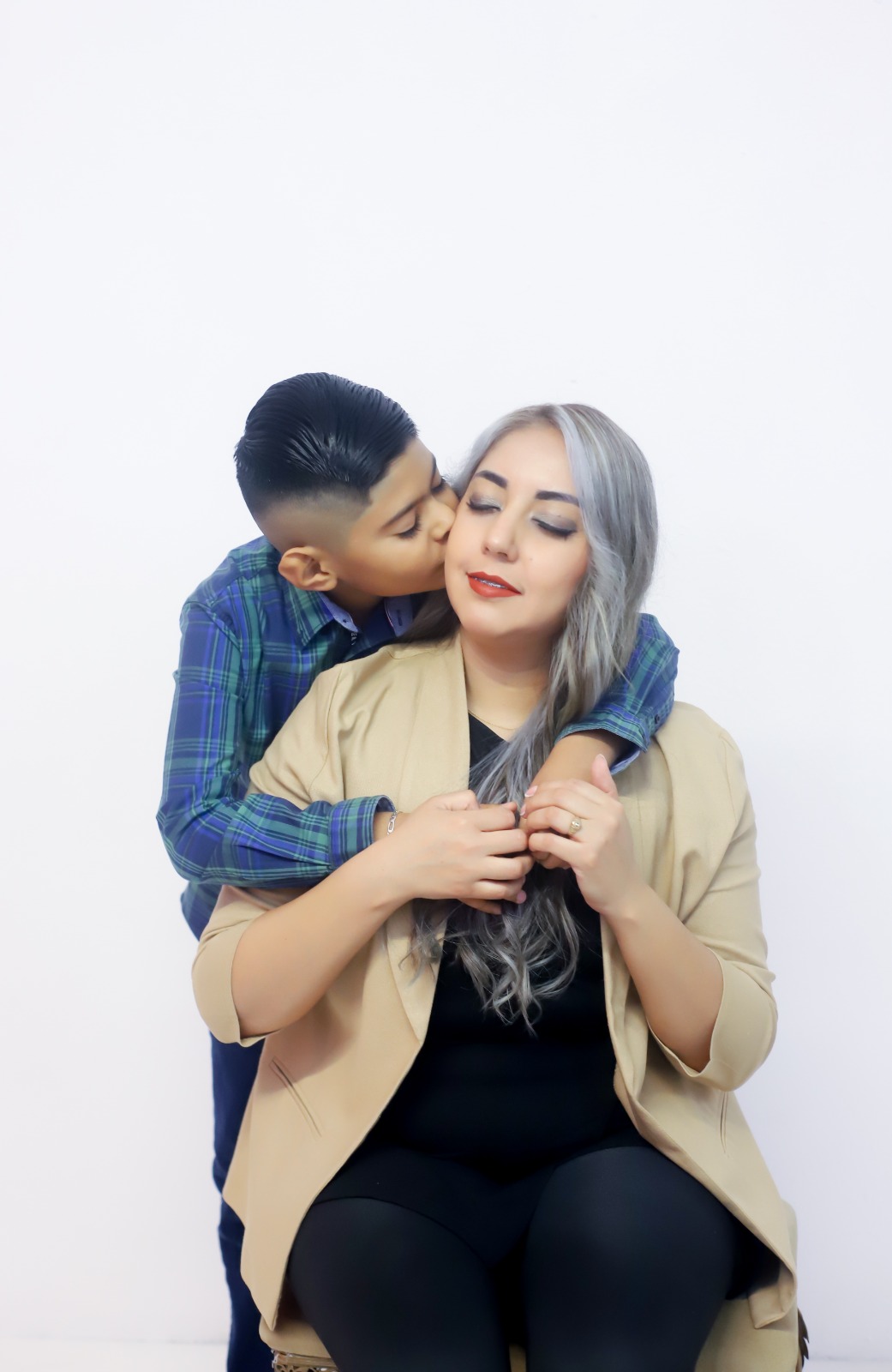 Niño abrazando a su mamá en una sesión de estudio sobre fondo blanco.
