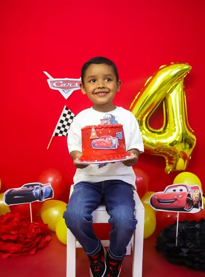 Niño sujetando su pastel de Cars junto al globo número cuatro.