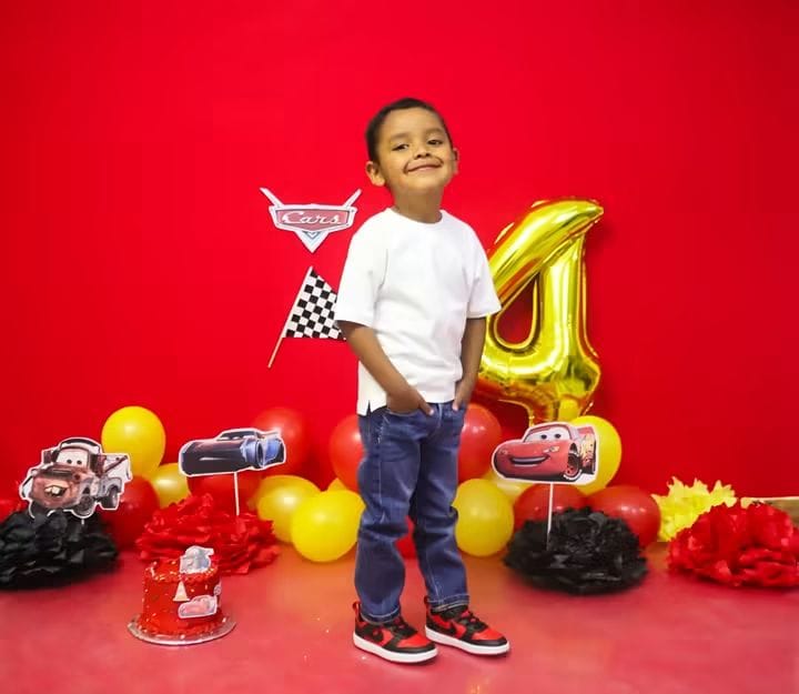 Niño de pie frente a la decoración de su fiesta de Cars.