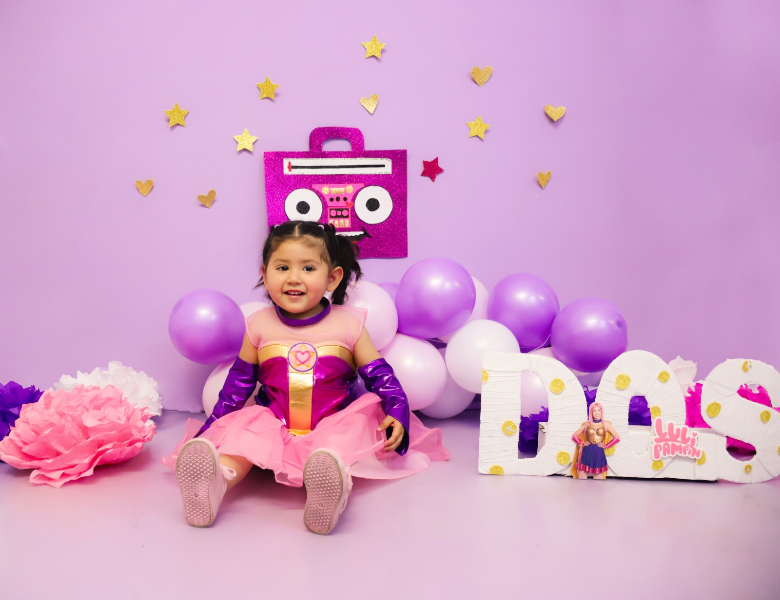 Niña disfrazada de princesa junto a letras decorativas en un set morado.