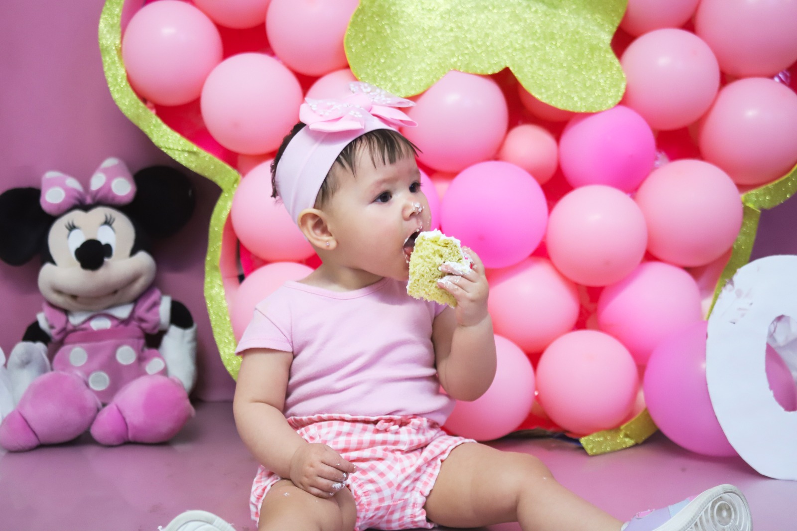 Bebé comiendo su pastel de primer año en un set rosa con globos.