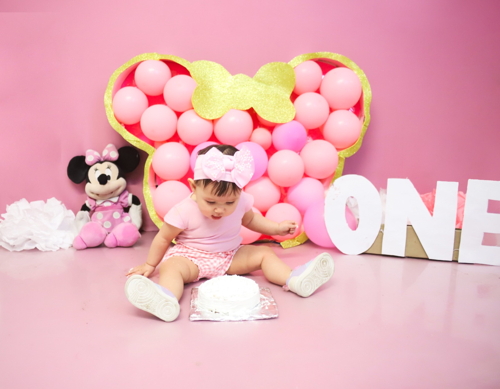 Bebé sentada frente a su pastel en un set rosa de primer año.
